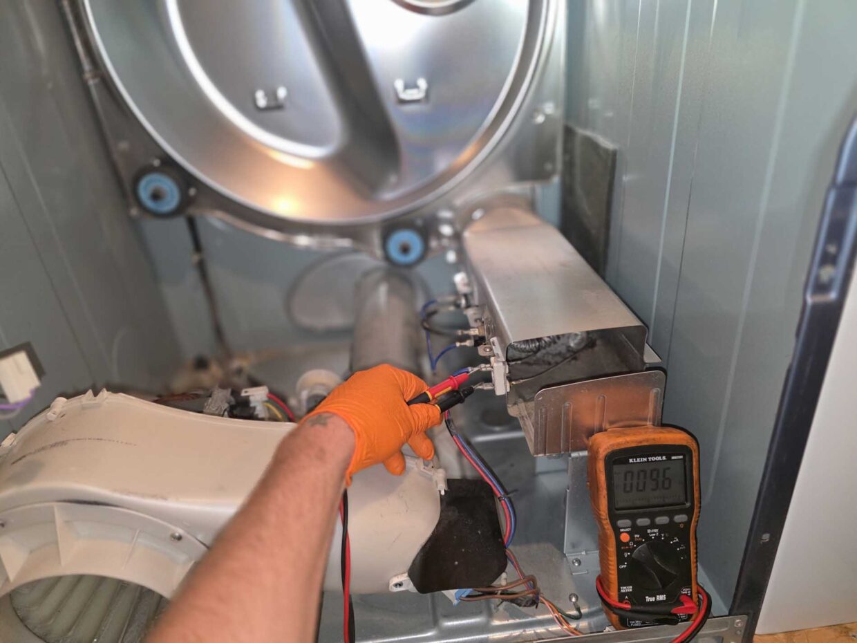 Gloved hands testing dryer components with a multimeter during a repair