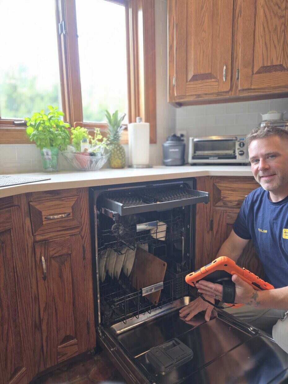 Technician repairing an open dishwasher in a wood-cabinet kitchen