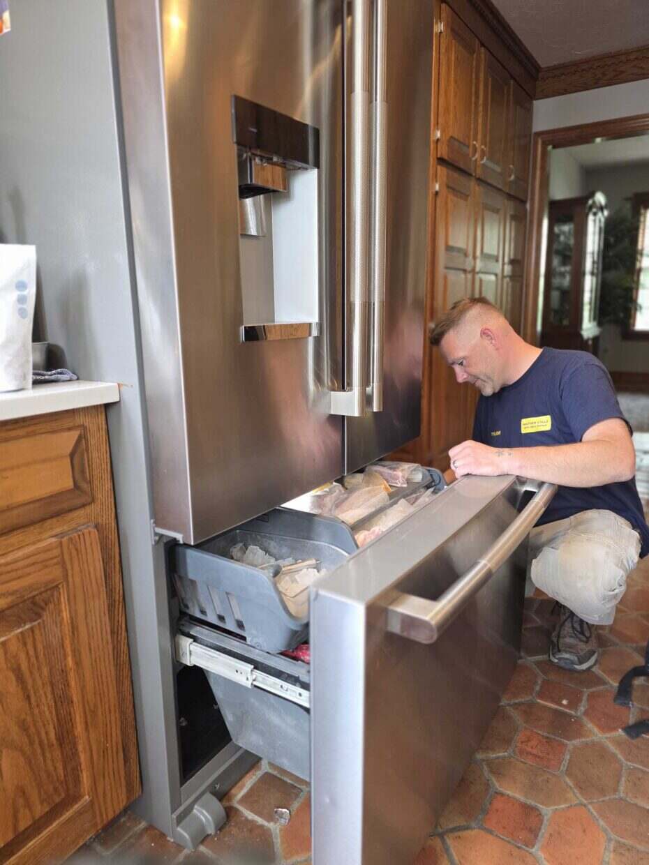 Technician servicing the open freezer drawer of a stainless steel French-door refrigerator