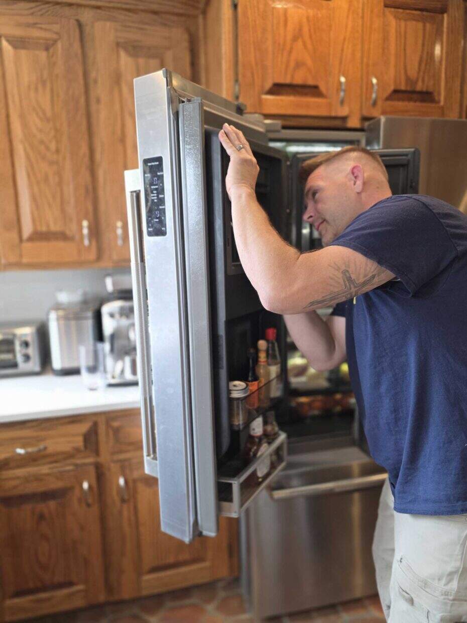 Technician inspecting an open French-door refrigerator in a home kitchen