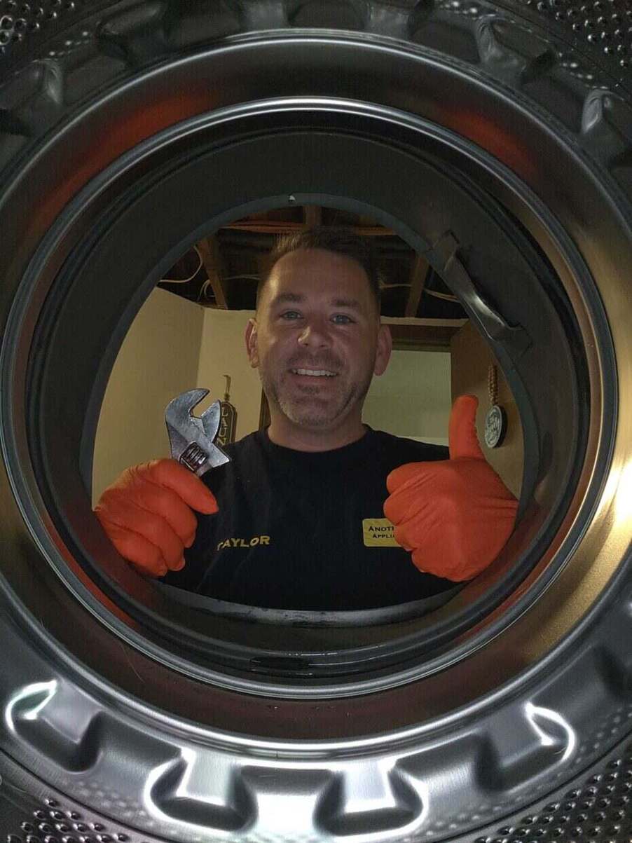 Technician giving a thumbs up through the open drum of a front-load washing machine