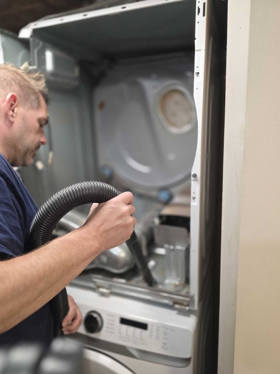 Technician vacuuming lint from inside the cabinet of a stacked laundry dryer