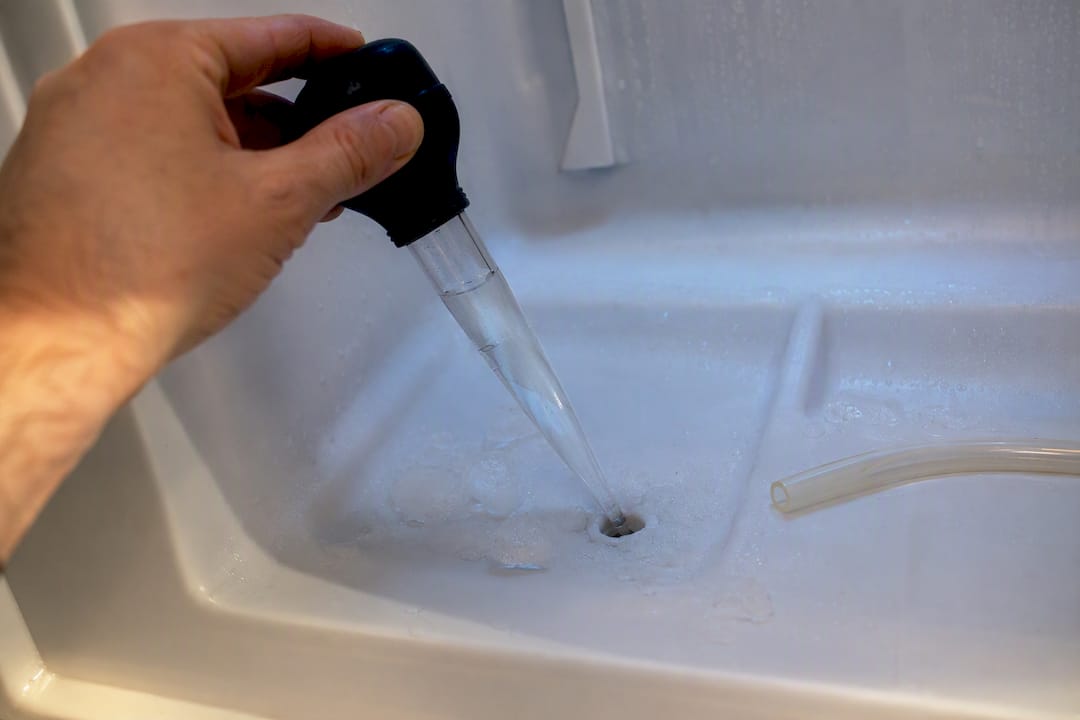Hands clearing an iced refrigerator drain